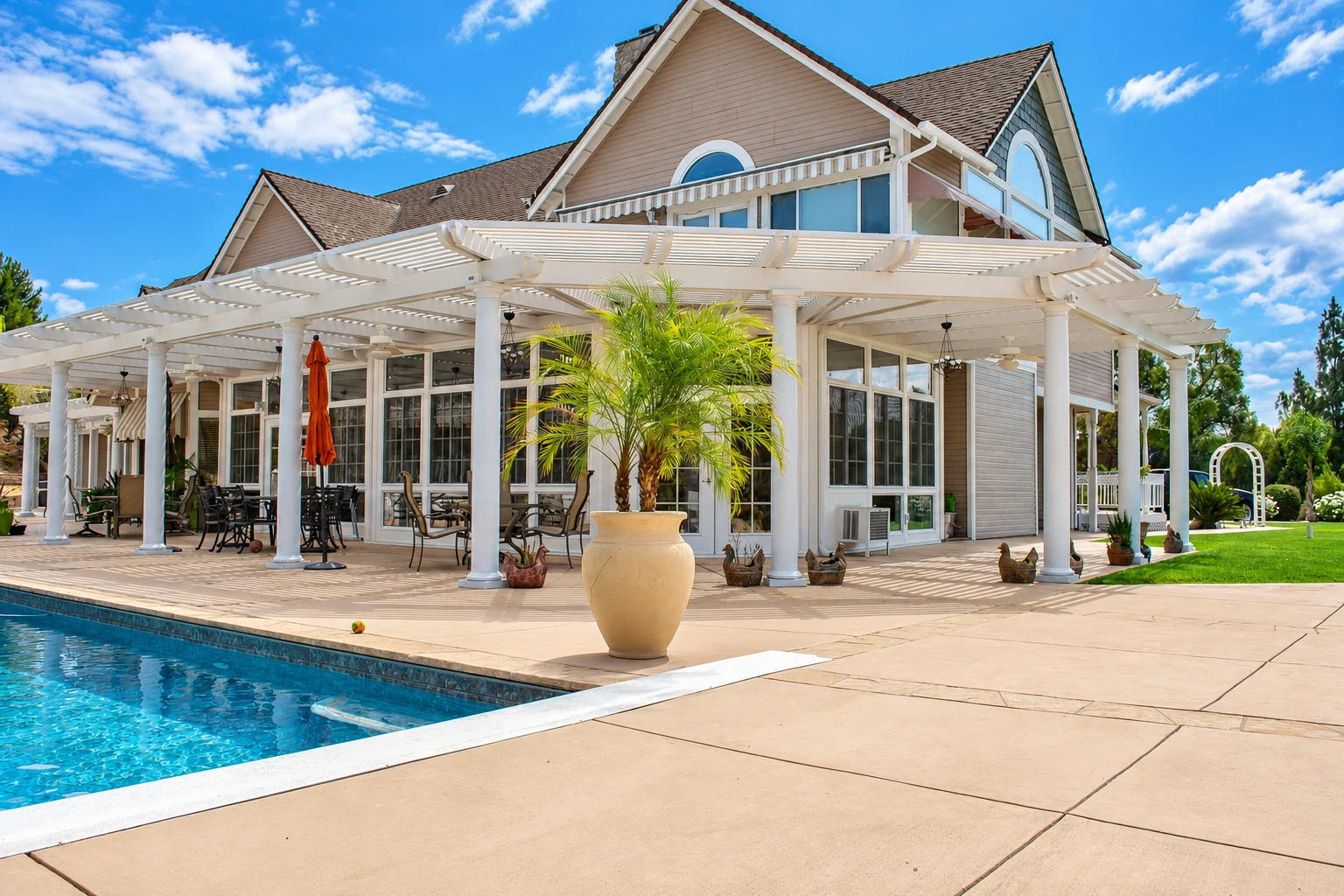 A large white pergola-style patio cover shades outdoor dining areas beside a swimming pool.