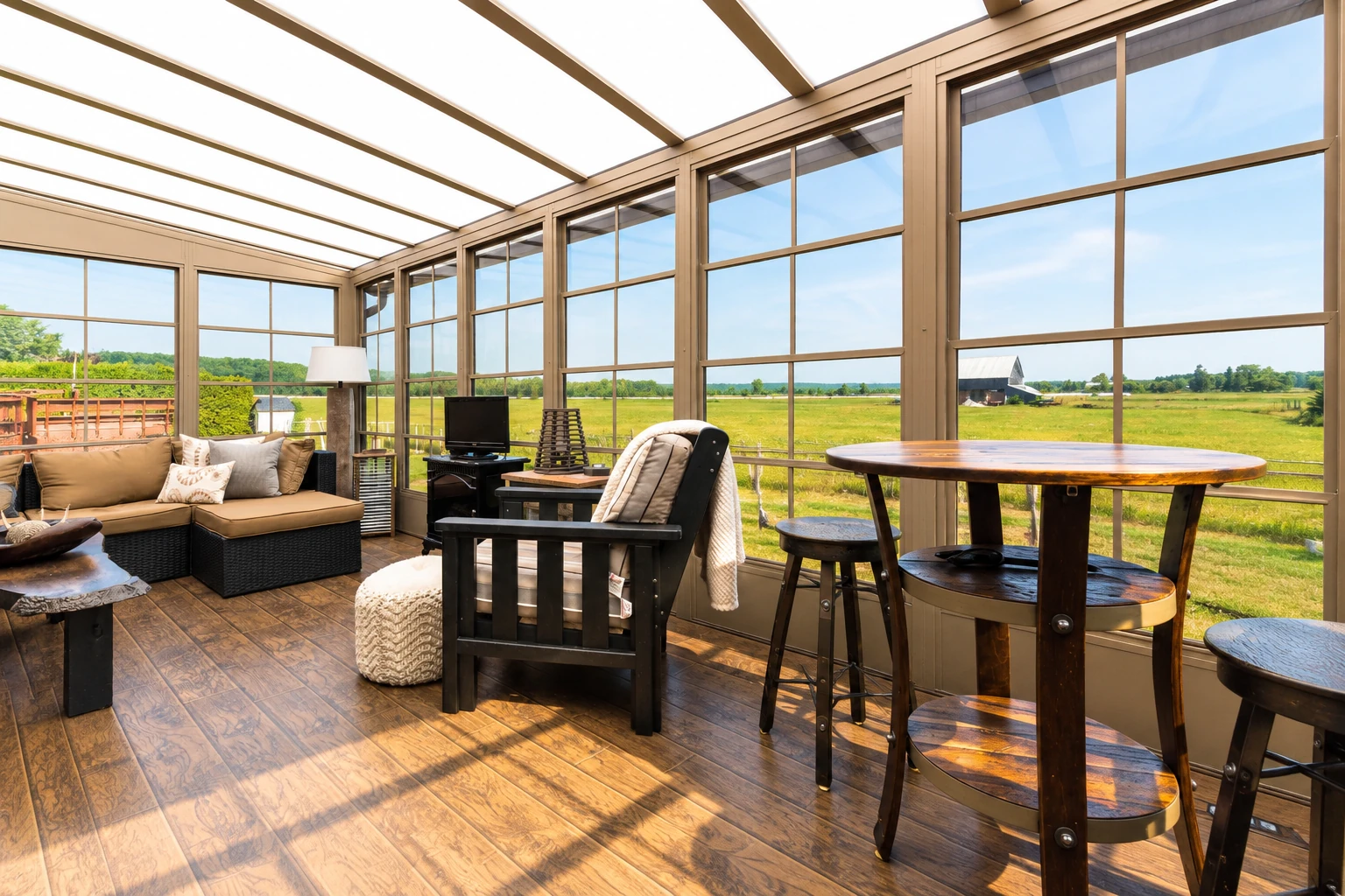 A furnished sunroom with tan-framed glass walls and a translucent roof overlooks an open field.