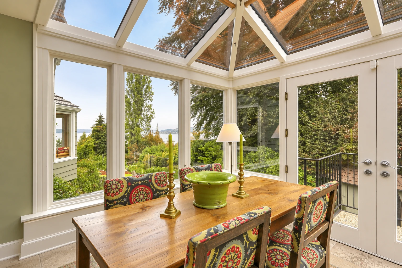 A sunroom with a glass-paneled roof, large windows, and a wooden dining table surrounded by patterned chairs.